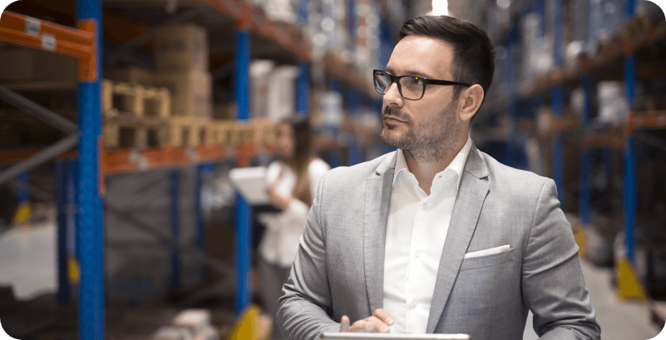 portrait-successful-businessman-manager-ceo-holding-tablet-walking-through-warehouse-storage-area-looking-towards-shelves