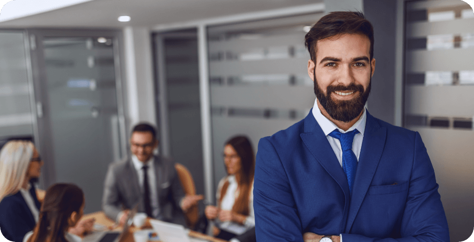 young-smiling-satisfied-businessman-suit-standing-boardroom-with-arms-crossed-background-his-colleagues-having-meeting