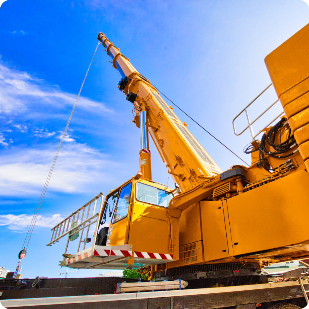 Yellow mobile hydraulic crane lifting materials at a construction site with a bright blue sky in the background