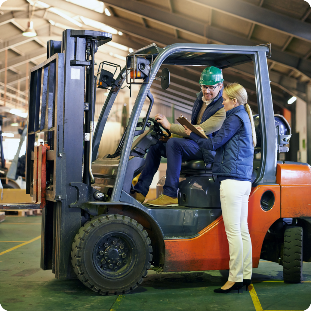 Forklift operator speaking with a supervisor holding a clipboard inside a warehouse, discussing logistics and safety procedures for efficient material handling
