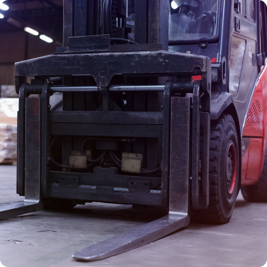 Front view of an industrial forklift with metal forks lowered, positioned on a warehouse floor for material handling tasks