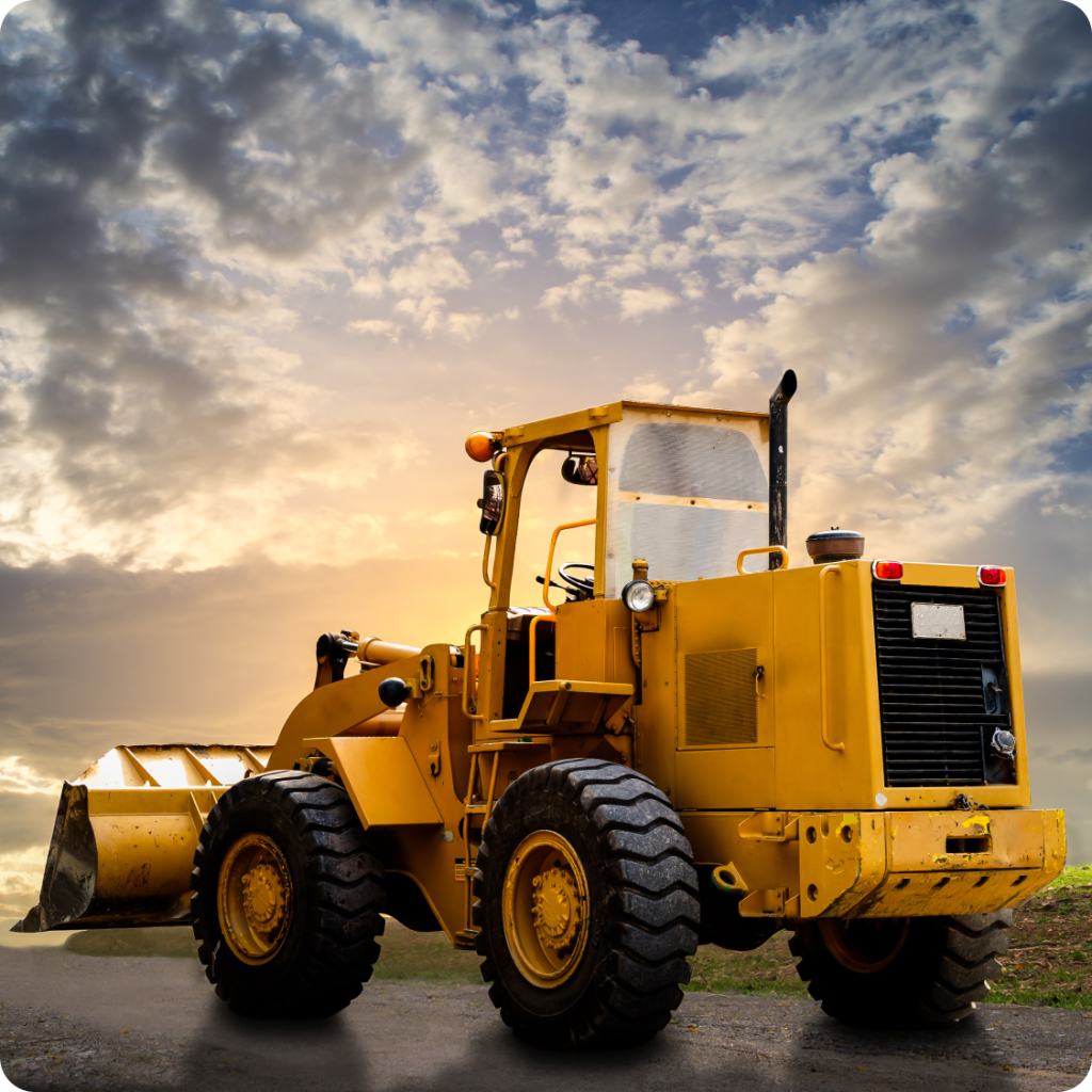 Yellow front loader tractor parked on a road during sunset with dramatic clouds in the sky, showcasing heavy machinery used for construction and farming