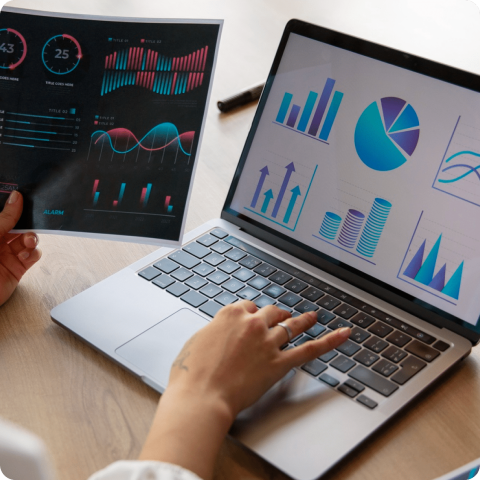 Analyzing Business Performance with Digital Reports and Analytics Close-up of hands analyzing business charts and graphs on a laptop and printed report for data-driven decision making