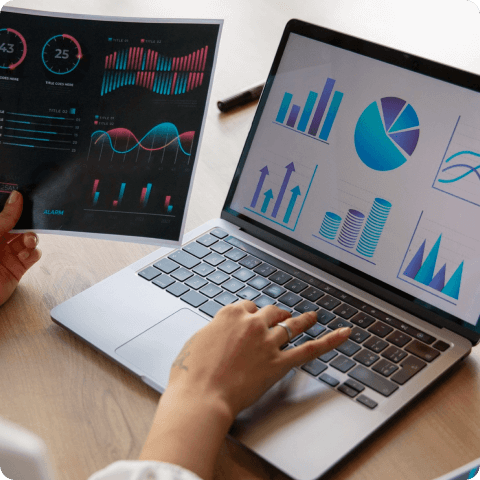 Close-up of hands analyzing business charts and graphs on a laptop and printed report for data-driven decision making