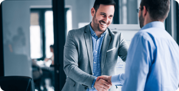 two-smiling-businessmen-shaking-hands-while-standing-office Closing a deal banner - men shaking hands
