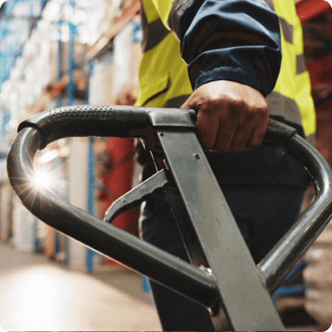 Close-up of a warehouse worker’s hand operating a pallet jack in an industrial storage facility